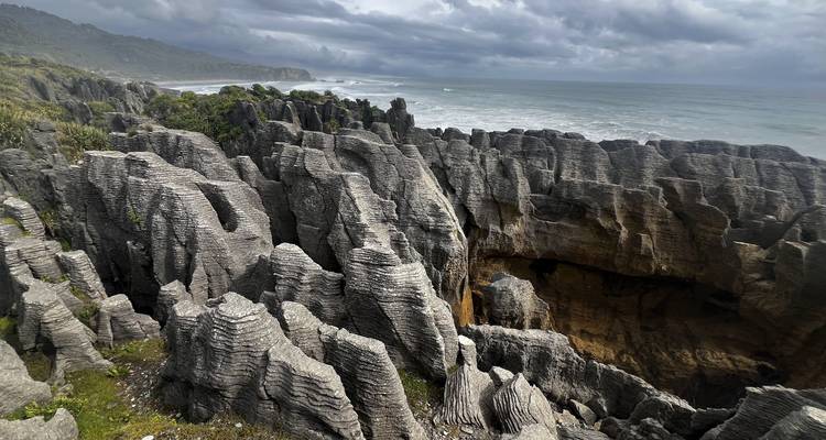Dramatische kalksteenformaties Pancake Rocks stapelen zich langs een robuuste kustlijn onder grijze, sombere luchten.