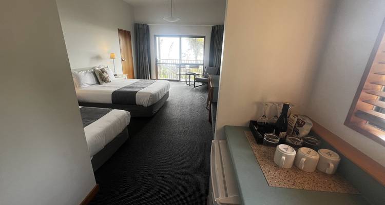 Eenvoudige moderne hotelkamer met twee bedden, balkon en theestation gezien vanuit de gang.