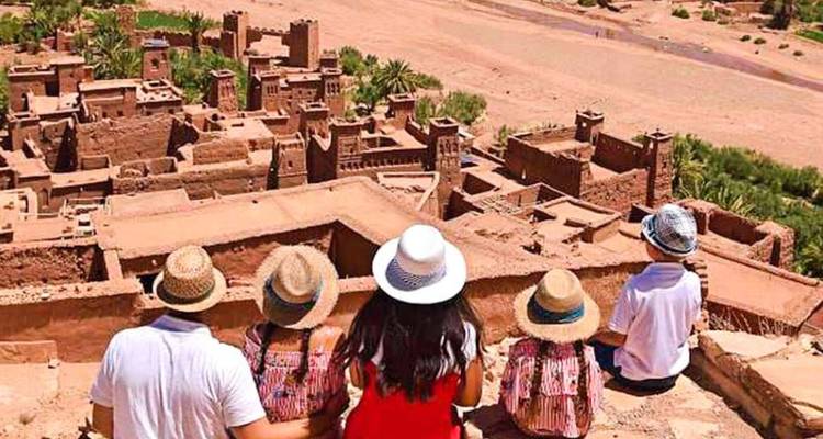 Familie met zonnehoedenzitten op een uitkijkpunt met uitzicht op de aarden kasbah's van Ait Benhaddou.