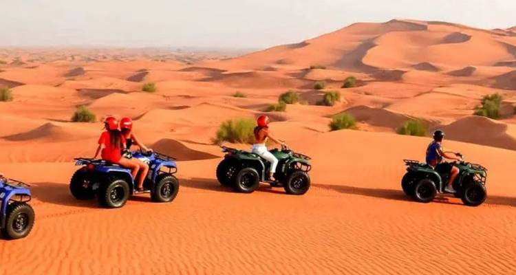 Rij met quads en coureurs met helmen die over rollende oranje zandduinen rijden.