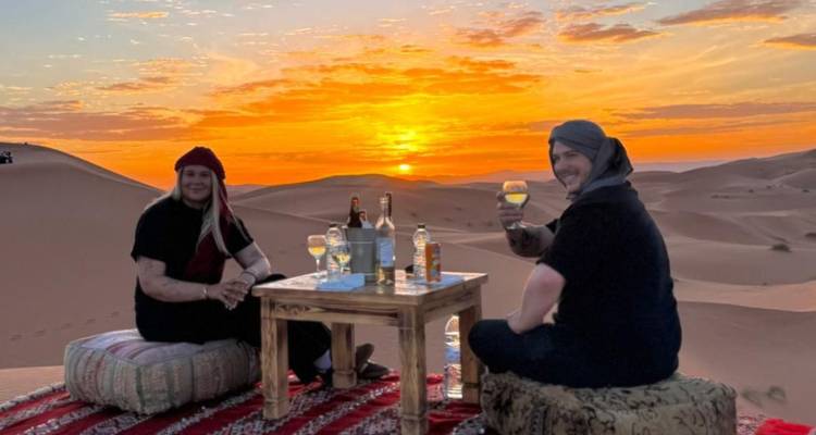 Stel geniet van zonsondergang dranken aan een klein tafeltje op zandduinen met een levendige oranje lucht.