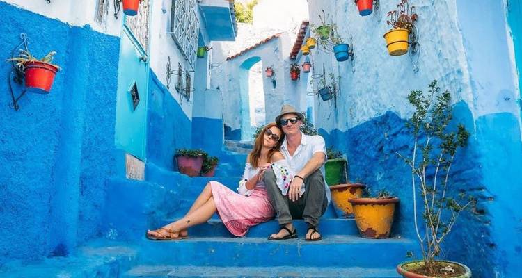 Stel zit op felblauwe trappen omgeven door kleurrijke bloempotten in het blauwe medina van Chefchaouen.