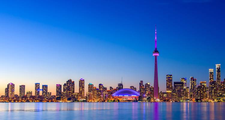 Twilight skyline van Toronto met de verlichte CN Tower in magenta die zich weerspiegelt in het Ontariomeer.