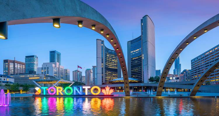 Avondview van Toronto-bord dat in regenboogkleuren gloeit naast reflectiepool onder moderne bogen.