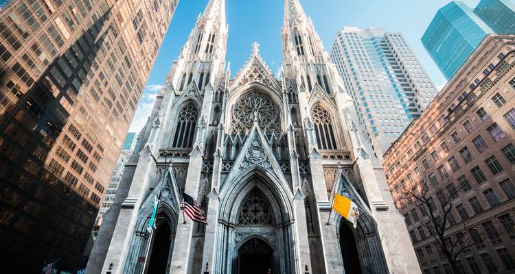 Upward view of the ornate Gothic façade of St. Patrick’s Cathedral framed by Manhattan skyscrapers.
