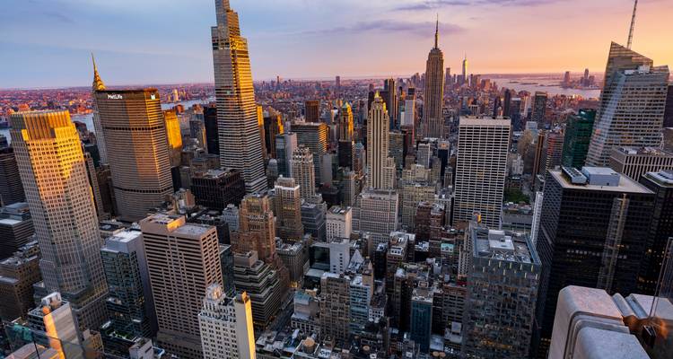 Panoramic sunset over Manhattan’s dense skyline with golden light on skyscrapers and distant harbour.