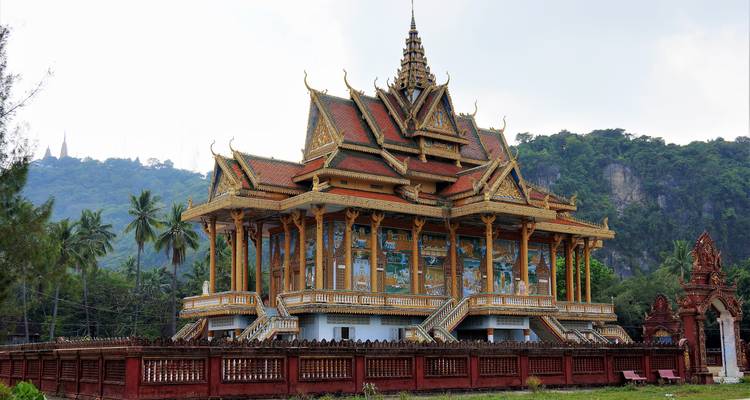 Pagode ornée au sommet d'une colline entourée de verdure luxuriante et de falaises en Cambodge rural.