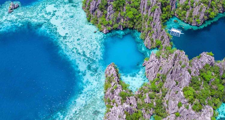 Vue aérienne dynamique des lagon turquoise, des falaises calcaires et d'un bateau à balancier à Palawan