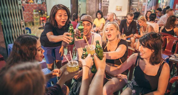 Groupe de jeunes voyageurs trinquant avec des bouteilles de bière dans un bar de rue animé