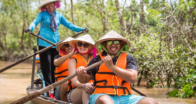 Des touristes portant des chapeaux coniques naviguant en pagayant dans une étroite barque en bois sur une rivière boueuse