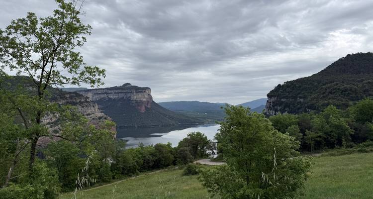 Réservoir calme reflétant des falaises escarpées et des collines verdoyantes sous un ciel nuageux.