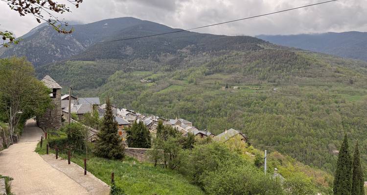 Petit hameau de montagne aux toits de pierre dominant une vaste vallée boisée sous des nuages menaçants.