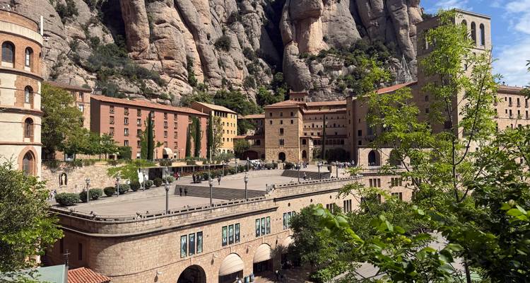 Historische Montserrat-kloostergebouwen tegen dramatische gezaagde rotskliffe onder de felle zon.