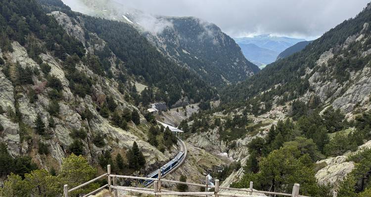 Steil Pyreneeëndal met een tandradbaan die zich door dennebeboste hellingen onder lage wolken slingert.