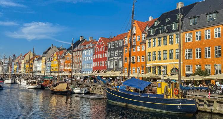 Helder zonnig uitzicht op het Nyhavn-kanaal met levendige rij huisjes en boten die in het water weerspiegelen.