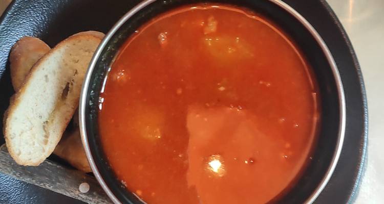 Kom heerlijke rode tomatensoep met stukjes geroosterd brood op een donker bord