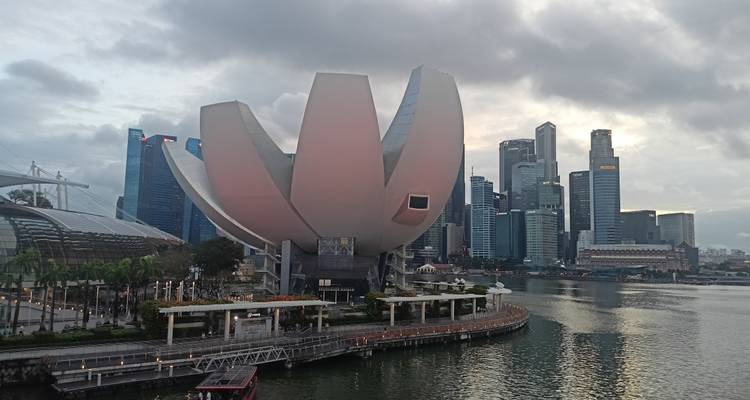 Ikonisches, lotusförmiges ArtScience Museum mit Singapurs Marina Bay Skyline und Uferpromenade bei Einbruch der Dunkelheit