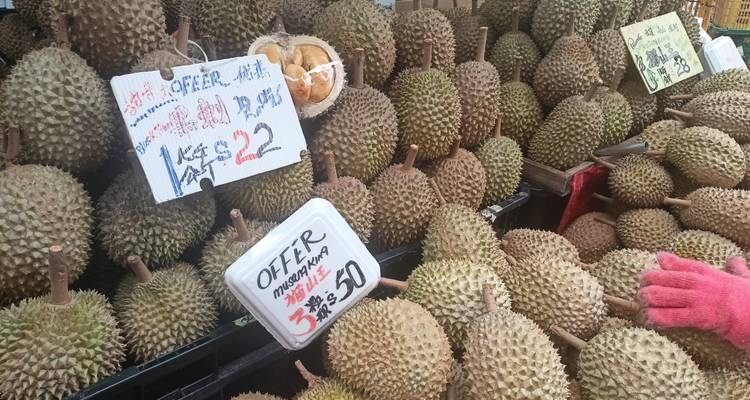 Marktstand mit hoch aufgestapelten stacheligen Durianfrüchten und handgeschriebenen Preisschildern mit Sonderangeboten