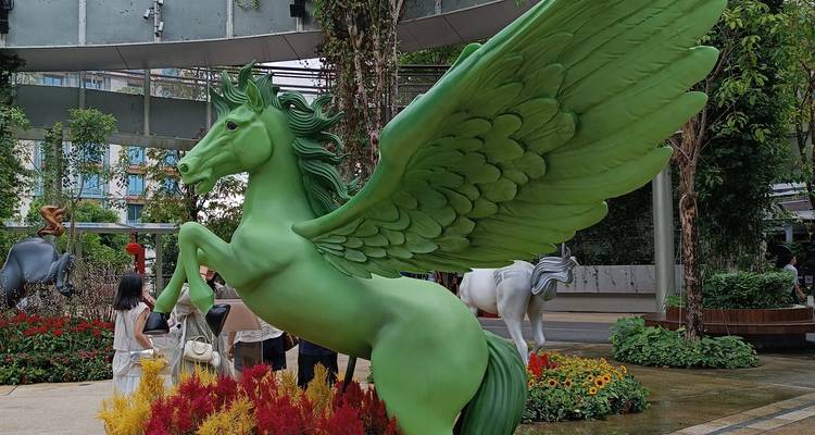 Große grüne Pegasus-Skulptur, aufbäumend inmitten farbenfroher Blumenbeete in einer Freiluftgartenanlage