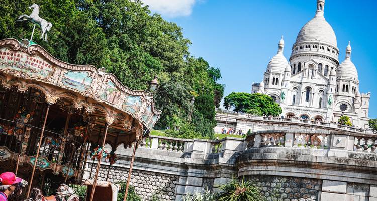 Carrousel fantaisiste au premier plan avec la Basilique du Sacré-Cœur perchée sur la colline au-delà de verdure luxuriante.