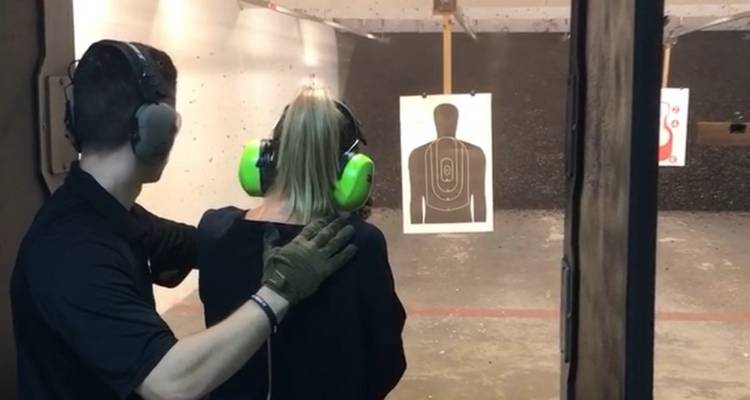 Un homme assiste une femme qui vise une cible en silhouette à l'intérieur d'un champ de tir; tous deux portent des protège-oreilles vert vif.