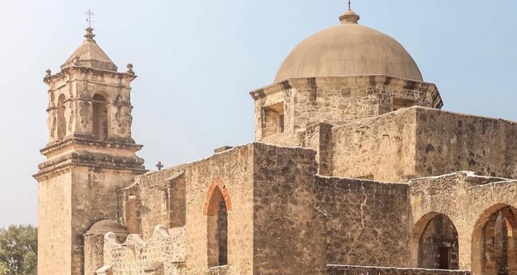 <p>Historic stone mission with bell tower and dome stands beneath a clear blue Texas sky.</p>

Mission historique en pierre avec clocher et dôme s'élevant sous un ciel bleu clair du Texas.