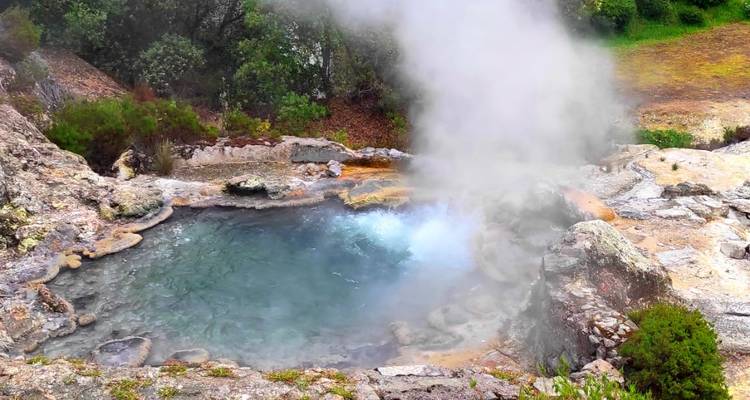 Actief warm bronnen zwembad dat stoom uitstoot en borrelend turkoois water in een vulkanische omgeving.