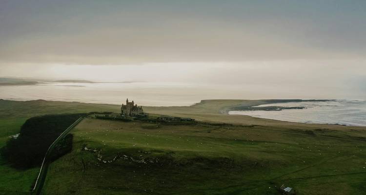 Stemmige luchtfoto van kasteel aan winderige kust met mistige zee en vlak landschap.