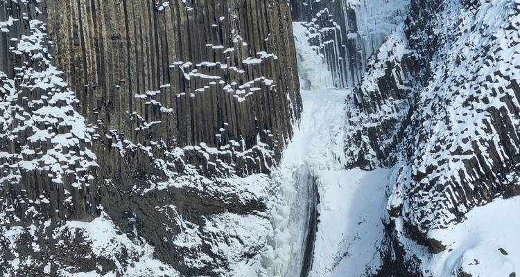 Des colonnes de basalte vertical recouvertes de neige à côté d'une cascade de chute d'eau gelée.