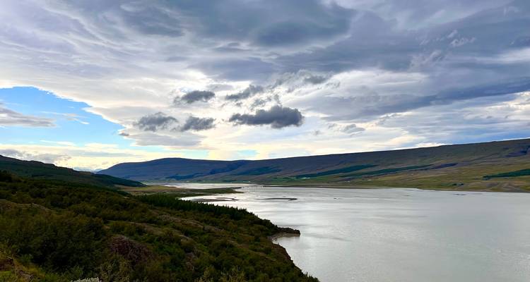 Vaste fjord ou lac aux pentes boisées sous des nuages superposés dramatiques.