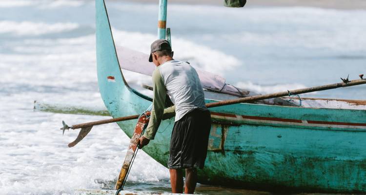 Lokale visser die een traditionele turquoise uitlegger boot op een rustig strand verzorgt.
