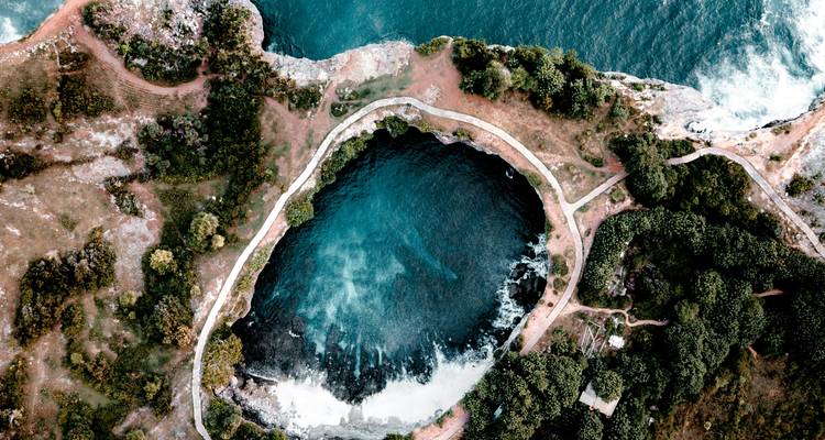 Drone-opname van het cirkelvormige getijdenplas Angel's Billabong omgeven door een rotsachtige kustlijn.