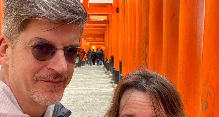 Een middelbare echtpaar dat een selfie maakt in de beroemde tunnel van felgele torii-poorten.