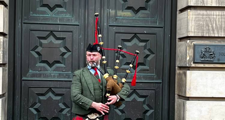 Joueur de cornemuse écossaise en tenue traditionnelle se produisant devant des portes en bois ornées