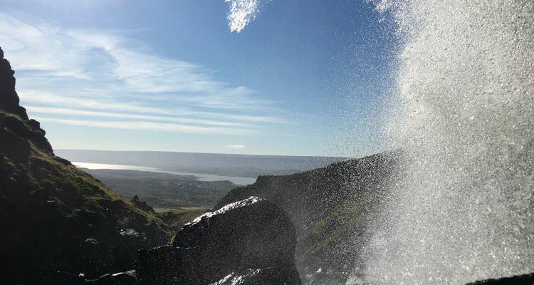Embruns d'une cascade rétroéclairés par le soleil avec vue sur la côte et le ciel au-delà.