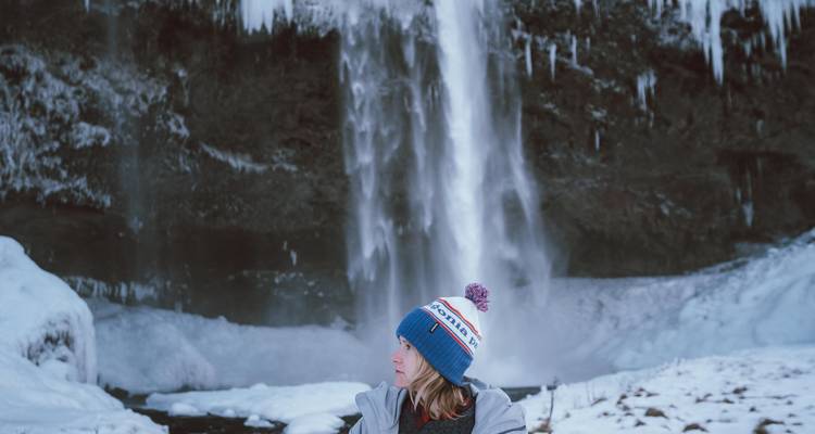 Femme portant un bonnet d'hiver regardant de côté avec une cascade gelée en arrière-plan.