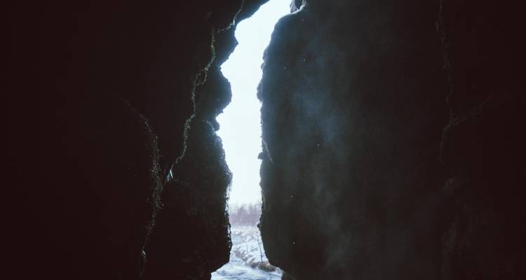 Entrée de grotte sombre avec une lumière diurne brillante et brumeuse au-delà des rochers.