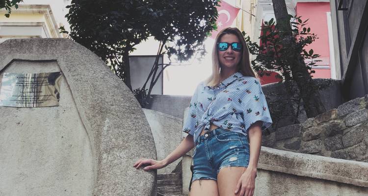 Une femme en short en denim se tient sur un escalier en pierre à Istanbul avec des drapeaux turcs accrochés à proximité.