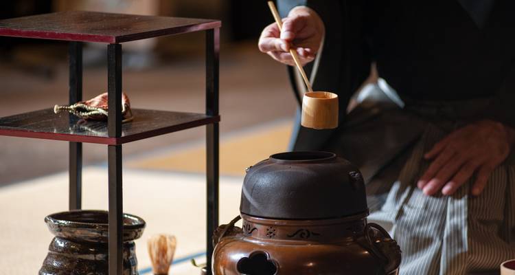 Close-up van een traditionele Japanse theeceremonie met een gelakte lepel boven een ijzeren ketel.