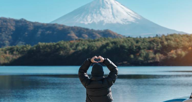 Reiziger vormt met zijn handen een hartje terwijl hij naar de met sneeuw bedekte Mount Fuji kijkt aan de overkant van het meer.