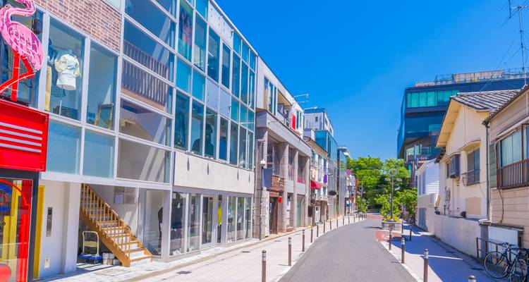 Helder, modern boetiekstraatje met glazen gevels onder een felblauw firmament in Tokio.