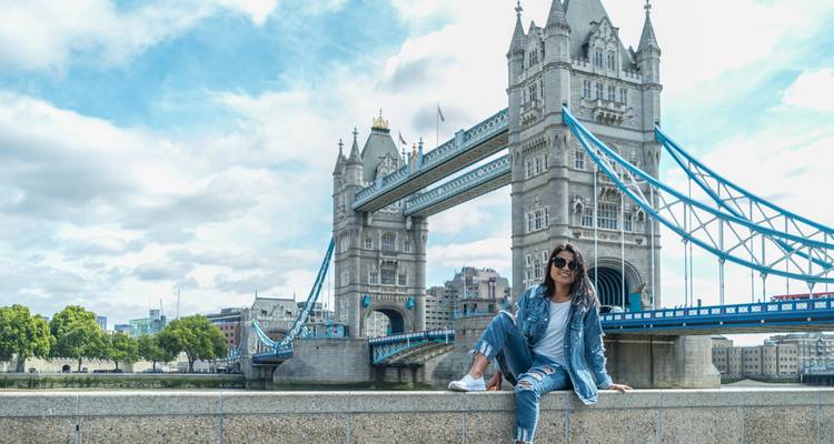 Une jeune femme en jean est assise sur un rebord de pierre avec le Tower Bridge s'étendant sur la Tamise derrière elle.