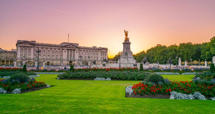 Le Palais de Buckingham et le Mémorial Victoria encadrés par des jardins formels colorés au coucher du soleil.