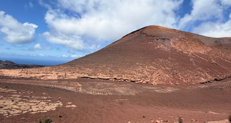 Cône volcanique rouge semblable à Mars et plaine désertique dans le parc national de Timanfaya sous un ciel bleu