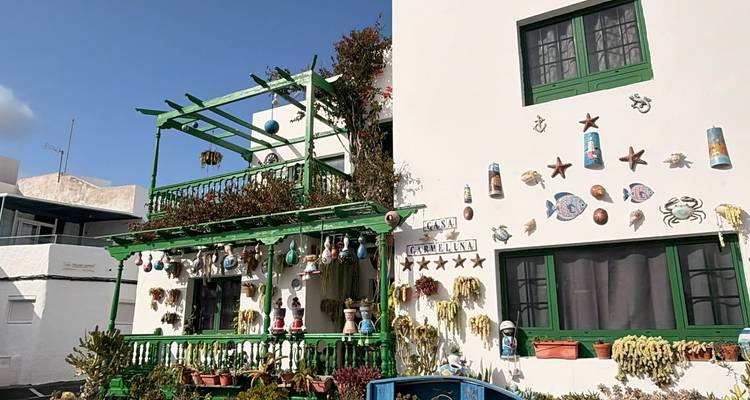 Una casa blanca peculiar decorada con balcones verdes, adornos con tema marino y macetas colgantes.