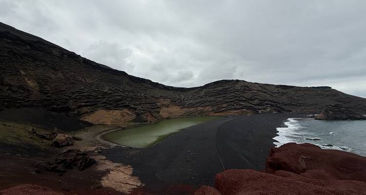 Vista amplia de la laguna verde en El Golfo con acantilados rojos y negros escarpados y olas que se estrellan.