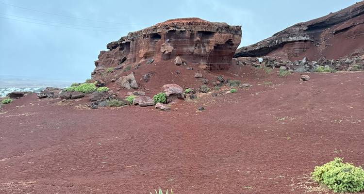 Una impresionante formación volcánica roja que se alza desde una llanura de ceniza carmesí.