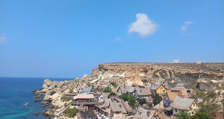 Les bâtiments en bois colorés du village de Popeye nichés dans une crique rocheuse surplombant une mer bleue cristalline.