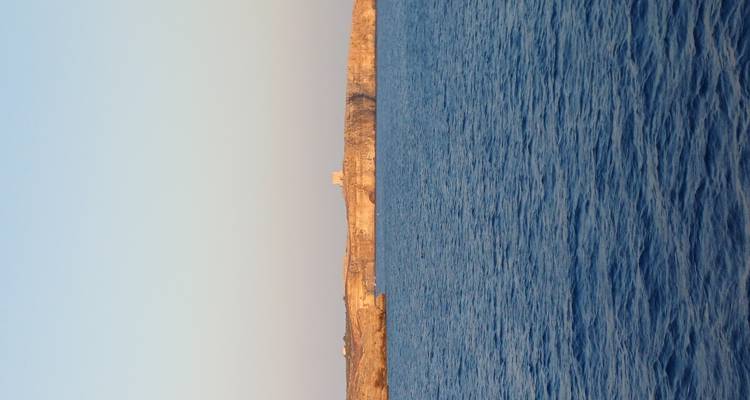Tour en pierre lointaine surplombant une mer calme en fin d'après-midi, baignée de lumière chaleureuse.