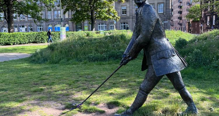 Statue en bronze d'un golfeur en plein swing située dans un parc urbain herbeux par une journée ensoleillée